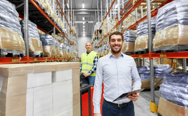 Fototapeta na wymiar logistic business, shipment and people concept - happy businessman with clipboard and worker loading goods by forklift at warehouse