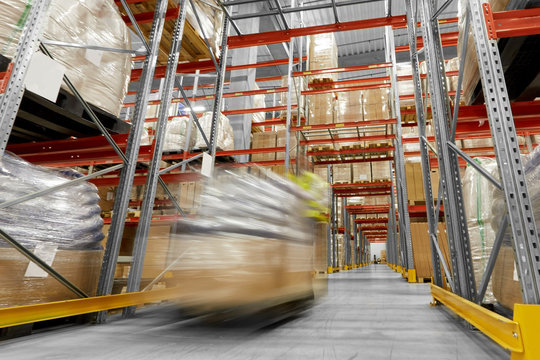logistic business, shipment and loading concept - motion blurred picture of worker carrying loader with goods at warehouse