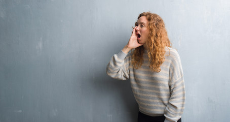 Fototapeta premium Young redhead woman over grey grunge wall shouting and screaming loud to side with hand on mouth. Communication concept.