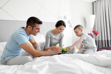 people, family and morning concept - happy child with toy tractor and parents playing in bed at...