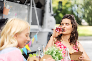 leisure and people concept - female friends drinking lemonade and eating at food truck