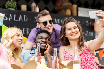 leisure and people concept - happy young friends with food and non alcoholic drinks and taking selfie at food truck