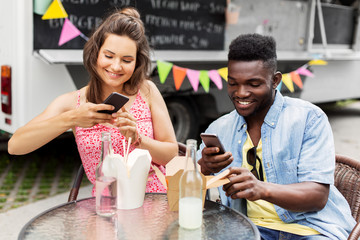 leisure, technology and people concept - happy mixed race couple photographing wok by smartphones at food truck
