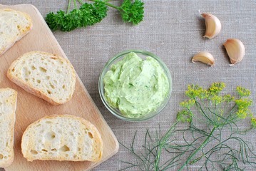 Appetizer garlic butter with herbs (dill, parsley), sliced bread. Top view on linen tablecloth.