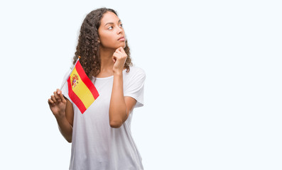 Young hispanic woman holding flag of Spain serious face thinking about question, very confused idea