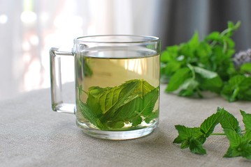 Fresh peppermint leaves tea served in glass cup on linen tablecloth.