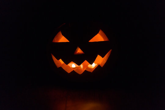 halloween and holidays concept - spooky jack-o-lantern or carved pumpkin lantern burning in darkness