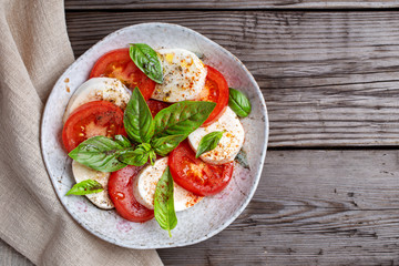 Caprese salad with mozzarella, basil and tomatoes on rustic wooden table. Top view with copy space