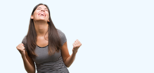 Obraz premium Young beautiful hispanic woman very happy and excited doing winner gesture with arms raised, smiling and screaming for success. Celebration concept.