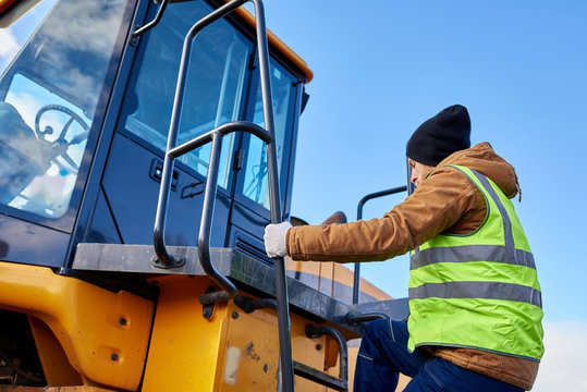 Portrait of bearded worker climbing ladder of heavy yellow truck against cold blue sky, copy space