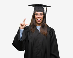 Young hispanic woman wearing graduated cap and uniform smiling and confident gesturing with hand doing size sign with fingers while looking and the camera. Measure concept.