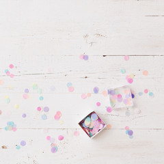 Top view on box full of colorful confetti on white wooden table or background.