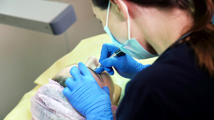 Cosmetologist applying permanent tattooing of eyebrows in beauty salon closeup. Modern microblading...