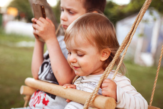 children sitting on a swing  with phone