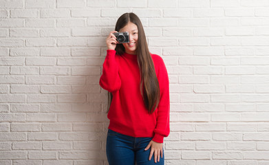 Young Chinese woman over brick wall holding vintage camera with a happy face standing and smiling with a confident smile showing teeth