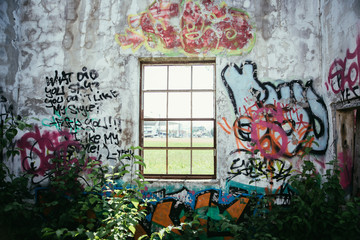 Fototapeta na wymiar Heruntergekommene Ruine mit Fenster, Graffiti und Pflanzen am Boden