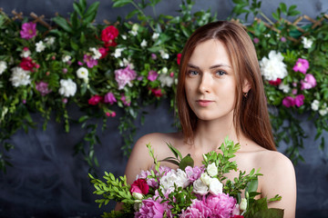 Skin care concept. Girl on calm face stands naked and holds flowers in front of chest. Beautiful woman with natural makeup takes pleasure while holds bouquet