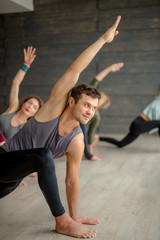 Group of caucasian women practicing yoga lesson with male instructor, standing in Warrior posture exercise, indoor fitness studio with grey background