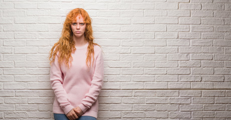 Young redhead woman standing over brick wall with serious expression on face. Simple and natural looking at the camera.