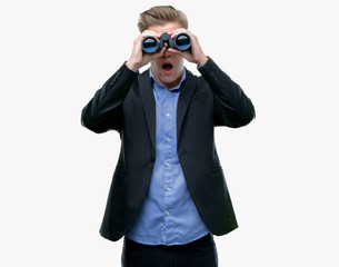 Young handsome blond man looking through binoculars scared in shock with a surprise face, afraid and excited with fear expression