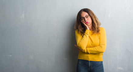 Middle age hispanic woman over grey wall wearing glasses thinking looking tired and bored with depression problems with crossed arms.