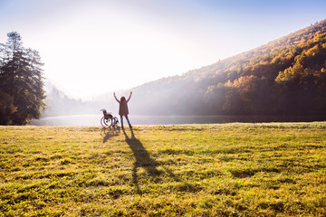 Senior woman standing by the wheelchair in autumn nature.