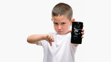 Dark haired little child holding broken smartphone with angry face, negative sign showing dislike...