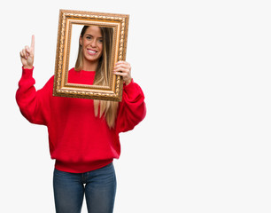 Fototapeta premium Beautiful young woman holding vintage frame surprised with an idea or question pointing finger with happy face, number one