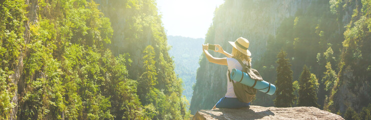 Girl hipster traveler takes pictures of nature on the background of mountains Tourist traveler on...