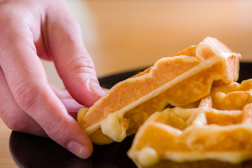 woman hands prepare waffle for serving process.waffle made from dough and batter.tasty dessert sweets waffle served on daylight in cafe background.waffle on black plate.
