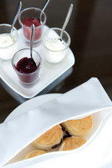 A tasty and delicious set of freshly baked scones with clotted cream and jam for afternoon tea or high tea party in elegant white setting. British way to relaxation. Natural light.