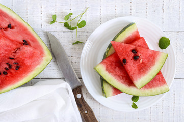 Ripe juicy red watermelon slices on a plate on a white wooden background.