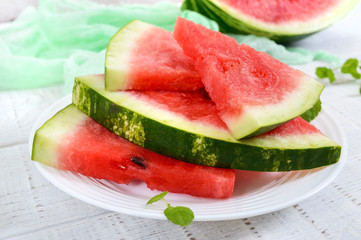 Ripe juicy red watermelon slices on a plate on a white wooden background.
