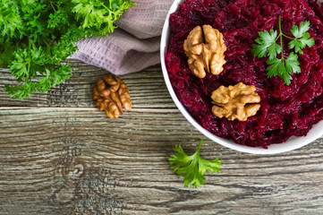 Boiled beetroot with nuts in a white bowl on a wooden background. Top view.