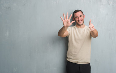 Young caucasian man over grey grunge wall showing and pointing up with fingers number six while...