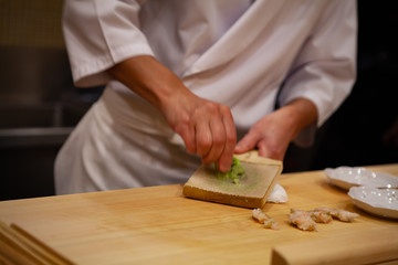 Professional sushi chef is using Oroshigane to grate fresh root of Wasabi or Japanese horseradish. Oroshigane or oroshiki is a Japanese style hand grater with the surface made from shark skin.