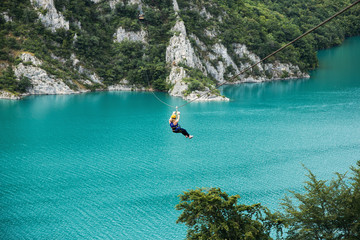Woman sliding on a zip line over the blue lake