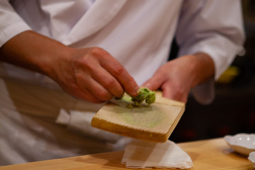 Professional sushi chef is using Oroshigane to grate fresh root of Wasabi or Japanese horseradish. Oroshigane or oroshiki is a Japanese style hand grater with the surface made from shark skin.