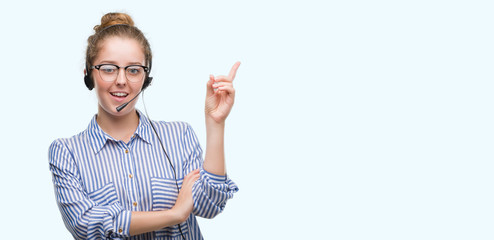 Young blonde call center operator woman very happy pointing with hand and finger to the side