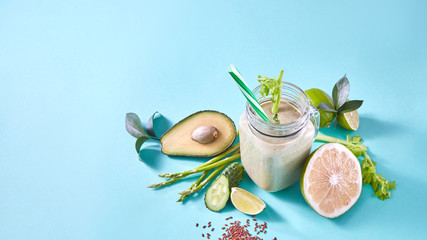 Green smoothie from organic vegetables , fruits, slices of lemon, lime, flax seeds in a glass bowl on blue paper background.