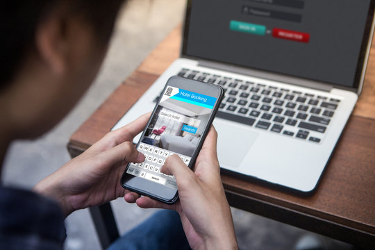 Businessman working on laptop and holding a smartphone in the hand with booking hotel travel app on screen in outdoor cafe