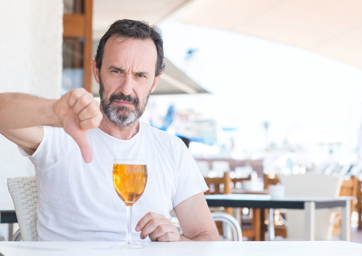 Handsome senior man drinking beer at restaurant with angry face, negative sign showing dislike with thumbs down, rejection concept