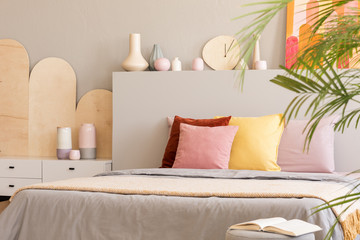Colorful cushions on bed with headboard next to cabinet in grey bedroom interior. Real photo