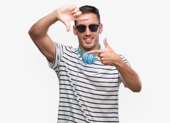 Handsome young man wearing headphones smiling making frame with hands and fingers with happy face. Creativity and photography concept.