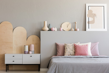 Pink pillows on grey bed in modern bedroom interior with poster and cabinet. Real photo