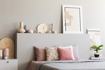 Poster on headboard of bed with pink cushions in grey bedroom interior with plant. Real photo