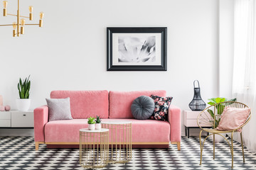 Glamour living room interior with a pink sofa, golden armchair and tables, painting and checkered...