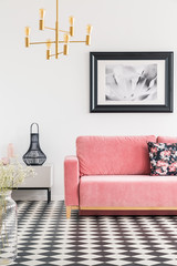 Checkered tiles in a living room interior with a pink sofa, painting and golden lamp. Real photo