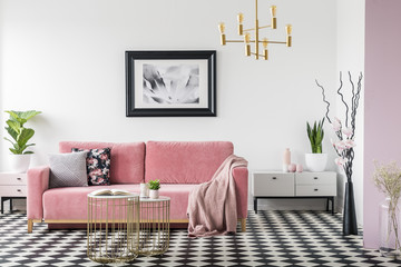 Real photo of a pastel living room interior with a sofa, coffee tables, painting, lamp, plants and branches in a vase