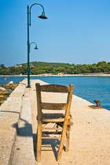 Old wooden chair on a pier in front of Koukounaries beach, morning at Skiathos island, Greece